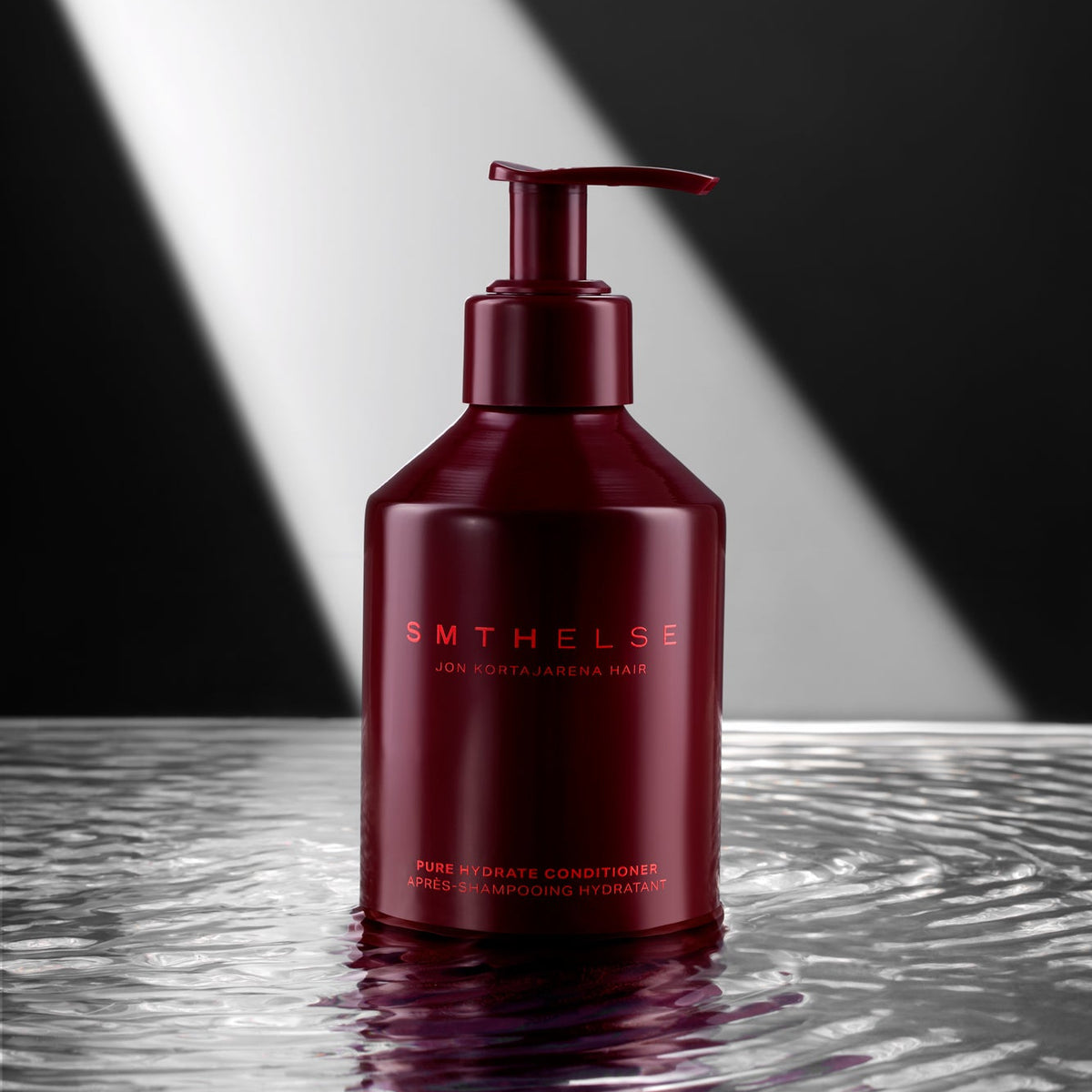 A dark red pump bottle of SMTHELSE hair conditioner standing on a reflective wet surface with a black and white geometric background.