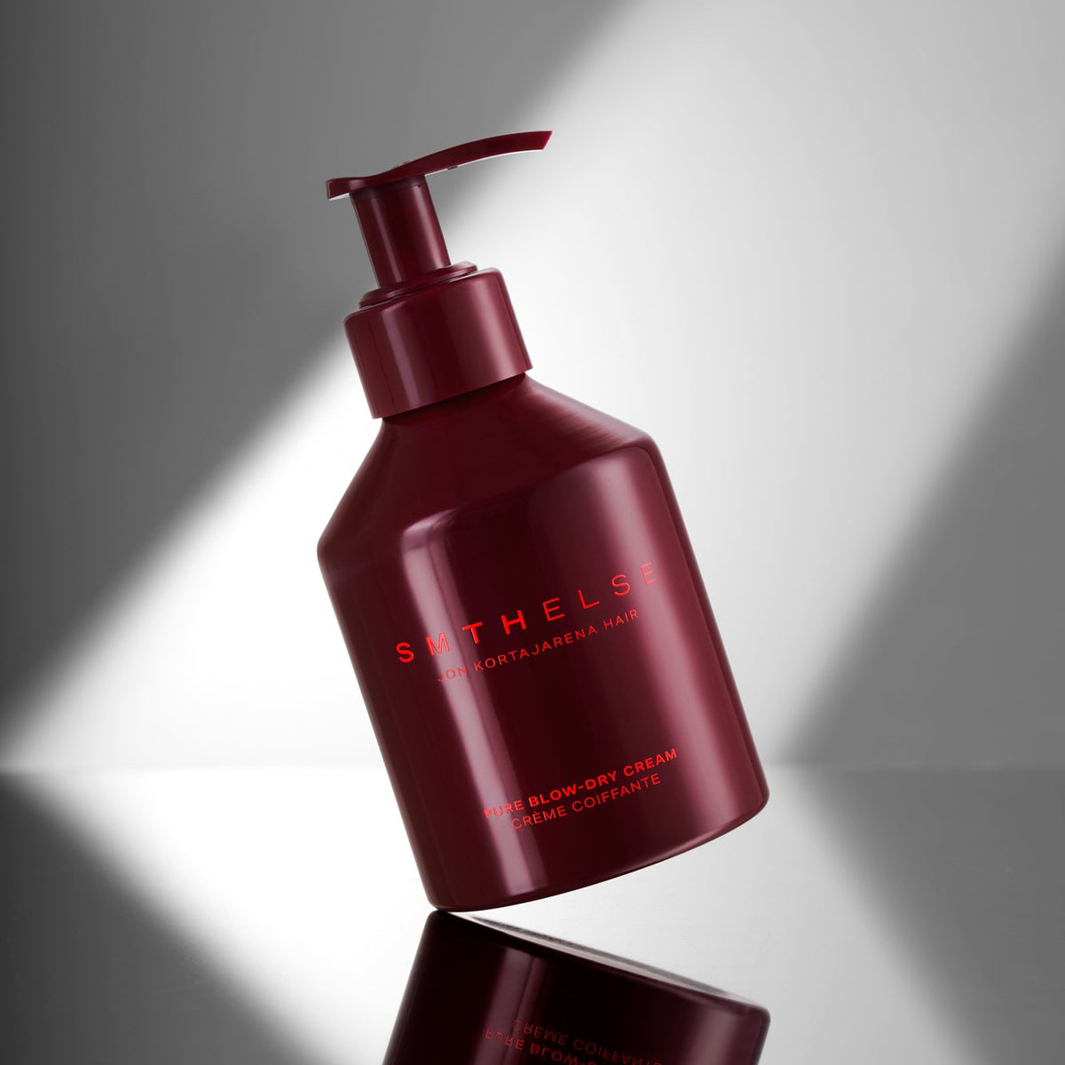 A dark red pump bottle of Bathels Body Butter Cream with gold lettering, shown on a reflective gray surface with dramatic diagonal light beams.
